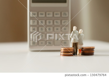 A miniature elderly couple and coins standing in front of a calculator. Pension. Retirement money image. A miniature elderly couple and coins standing in front of a calculator. Pension. Retirement money image. 130479764