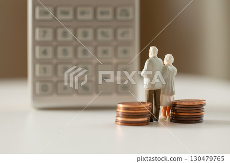 A miniature elderly couple and coins standing in front of a calculator. Pension. Retirement money image. A miniature elderly couple and coins standing in front of a calculator. Pension. Retirement money image. 130479765