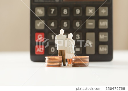 A miniature elderly couple and coins standing in front of a calculator. Pension. Retirement money image. A miniature elderly couple and coins standing in front of a calculator. Pension. Retirement money image. 130479766