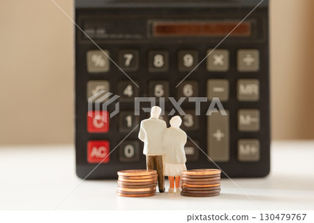 A miniature elderly couple and coins standing in front of a calculator. Pension. Retirement money image. 130479767