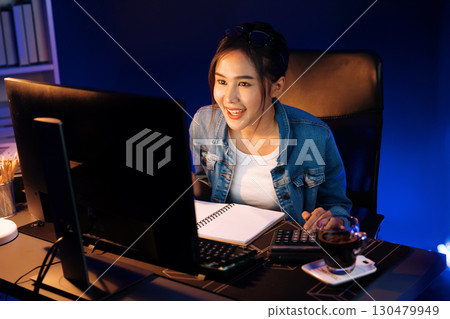 Smiling Asian creative looking pc of report and writing on notebook. Stratagem. Smiling Asian creative looking pc of report and writing on notebook. Stratagem. 130479949
