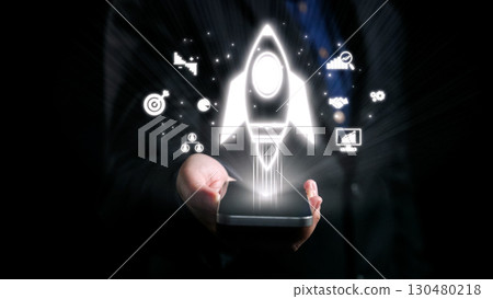 Creative Concept of Business Launch and Technology Growth Depicted by Hand Holding Smartphone with Rocket Icon and Graphic Symbols Representing Innovation. Qubit Creative Concept of Business Launch and Technology Growth Depicted by Hand Holding Smartphone with Rocket Icon and Graphic Symbols Representing Innovation. Qubit 130480218