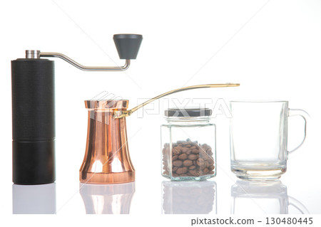 Close-up of a sleek black coffee grinder, a shiny copper cezve, a jar of coffee beans 130480445