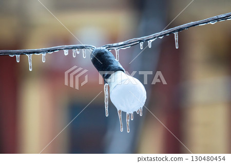 A single light bulb encased in ice, with icicles forming on a wire, set against a soft A single light bulb encased in ice, with icicles forming on a wire, set against a soft 130480454