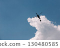 Silhouette of a firefighter helicopter against a background of white clouds and blue sky. 130480585