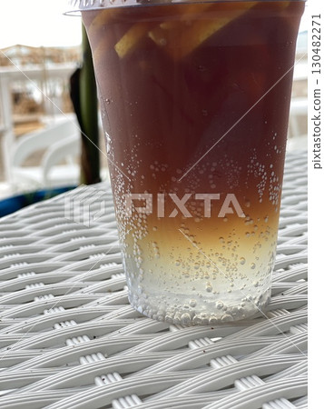 Iced tea in a clear plastic cup with lemon slices and bubbles, on woven table, seaside background 130482271