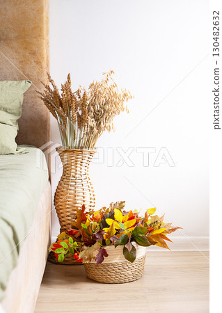 Wicker vase with dried wheat and oats next to decorative basket filled with colorful autumn leaves. 130482632