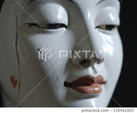 A cracked statue's delicate face evokes a sense of history and fragility 130482883