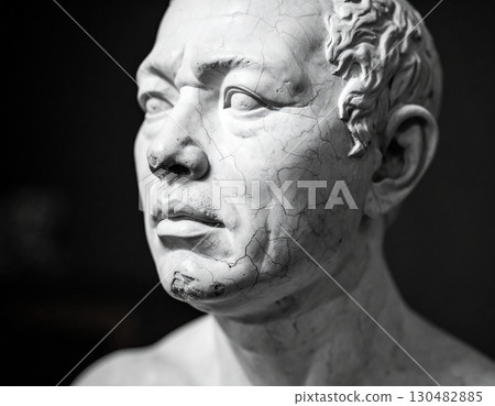 A cracked statue's delicate face evokes a sense of history and fragility 130482885