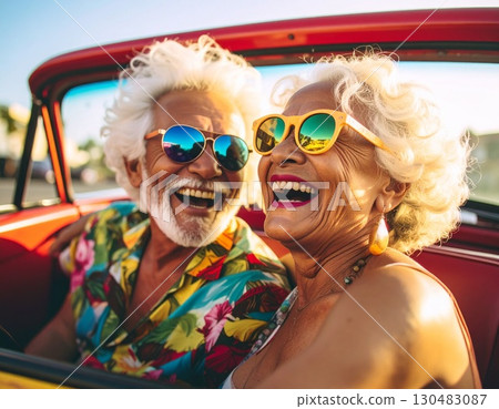 An elderly couple drives in a convertible, joyful together and smiling with a lovely backdrop. They have a happy drive on an open road. 130483087