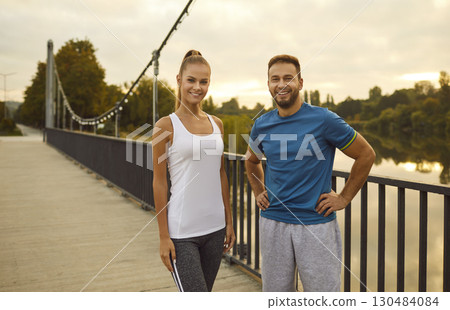 Handsome man and woman in sportswear standing on a bridge at sunset and smiling, close-up Handsome man and woman in sportswear standing on a bridge at sunset and smiling, close-up 130484084