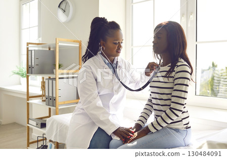 Female doctor with stethoscope examining woman's lungs and heartbeat in medical office. Female doctor with stethoscope examining woman's lungs and heartbeat in medical office. 130484091