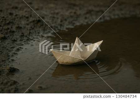A paper ship floats in a small puddle on the ground. 130484734