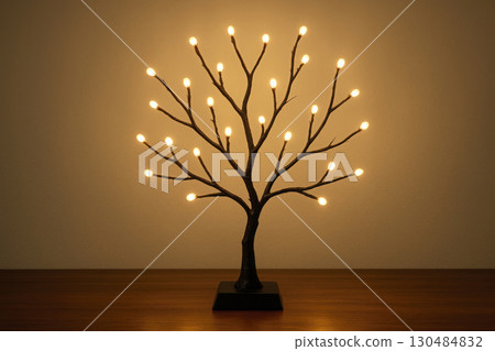 A tree-lamp with glowing bulbs turned on against the background of the wall. 130484832