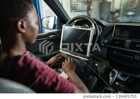 Car mechanic running diagnostics on a vehicle using a laptop Car mechanic running diagnostics on a vehicle using a laptop 130485703