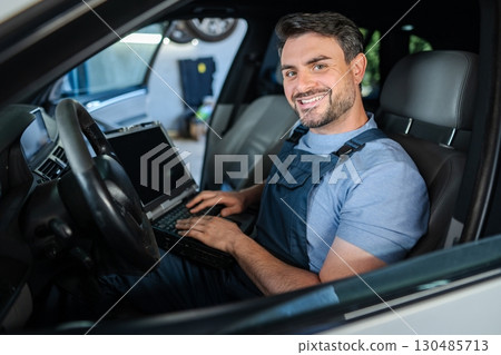 Smiling mechanic running diagnostics using laptop inside car 130485713