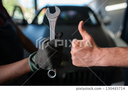 Mechanics holding wrench and making thumbs up sign in auto repair shop 130485714