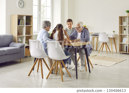 Grandparents and children are playing chess at the table in the living room at home 130486613