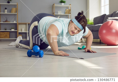 Tired overweight woman trying to do difficult push ups on an exercise mat at home 130486771