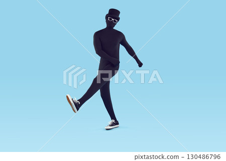 Faceless man wearing black bodysuit costume with hat and glasses walking on blue background. 130486796