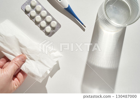 Person holding tissue with medications thermometer and water glass for cold 130487000