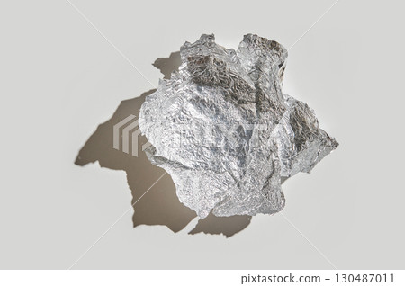 Silver aluminum foil crumpled into a ball with shadow on neutral background 130487011