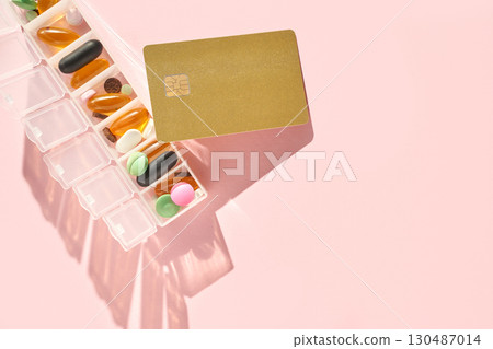 Gold credit card and weekly pill organizer with colorful capsules on pink 130487014