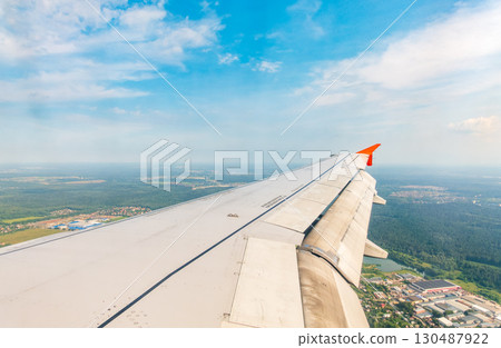 View of airplane wing, blue skies and green land during landing. Airplane window view. View of airplane wing, blue skies and green land during landing. Airplane window view. 130487922