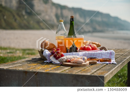 A cozy beach picnic in Normandy featuring French cidre, regional cheese, and fresh apples, set against a scenic coastal backdrop 130488009