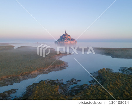 The iconic Mont Saint-Michel emerges through thick fog on a gloomy day, with its medieval village and abbey shrouded in mist on the Normandy coast The iconic Mont Saint-Michel emerges through thick fog on a gloomy day, with its medieval village and abbey shrouded in mist on the Normandy coast 130488014