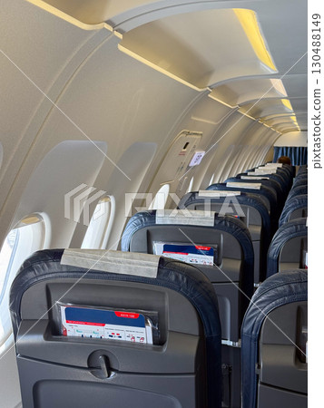 Empty black leather airplane seats next to a window with seatbelts placed on the cushions. Travel, aviation, and the arrangement of seating for passengers on modern flights. 130488149