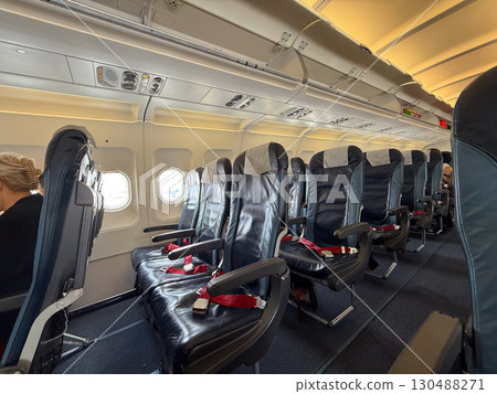 Empty black leather airplane seats next to a window with seatbelts placed on the cushions. Travel, aviation, and the arrangement of seating for passengers on modern flights. 130488271