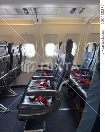 Empty black leather airplane seats next to a window with seatbelts placed on the cushions. Travel, aviation, and the arrangement of seating for passengers on modern flights. 130488273