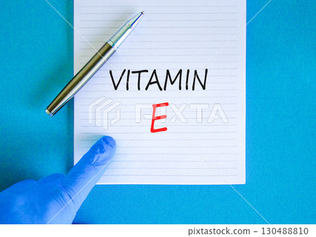 Vitamin E tocopherols symbol. Concept words Vitamin E on beautiful white note. Doctor's hand in blue medical glove. Beautiful blue background. Medical healthy lifestyle Vitamin E tocopherols concept. 130488810