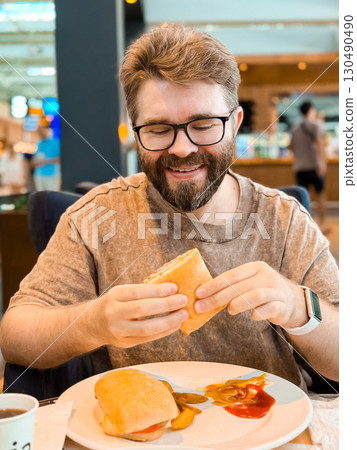 Smiling man holding sandwich with potato wedges in cafe interior. Lifestyle, leisure, and personality in modern dining culture. Smiling man holding sandwich with potato wedges in cafe interior. Lifestyle, leisure, and personality in modern dining culture. 130490490
