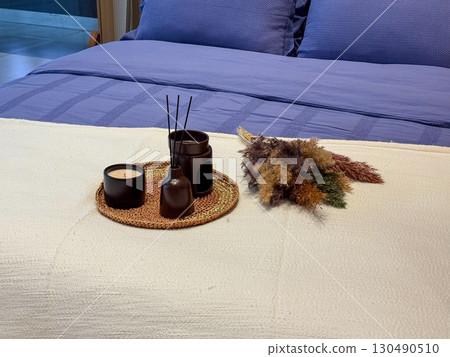 Bed with blue bedding and decorative set of candle, diffuser, and dried flowers. Comfort, lifestyle, and cozy atmosphere in modern interior design. 130490510