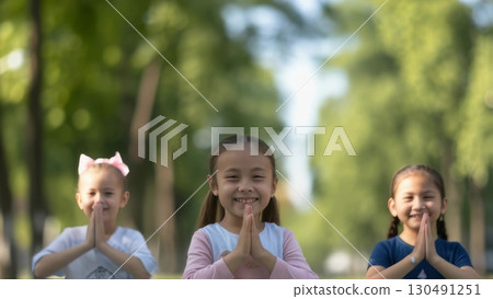 Young Thai girls performing traditional wai greeting, palms pressed together, bowing slightly with warm smiles, representing cultural respect in park landscape 130491251