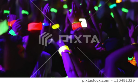 Concert crowd waving colorful glow sticks, generating electric atmosphere with synchronized movements, radiating music festival excitement and shared musical passion 130491329