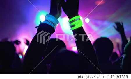 Concert crowd waving glowstick bracelets, cheering passionately during live music performance, sharing collective excitement and energy under vibrant stage lighting Concert crowd waving glowstick bracelets, cheering passionately during live music performance, sharing collective excitement and energy under vibrant stage lighting 130491359