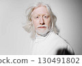 Portrait of an elderly man with long white hair and beard, wearing a white outfit against a soft gray background, conveying a sense of wisdom, serenity, and timeless elegance 130491802
