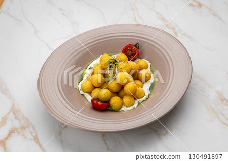 Gourmet potato balls with creamy sauce, herbs and cherry tomatoes on ceramic plate 130491897