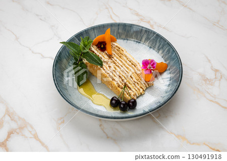 Layered honey cake slice with mint, cherries, and apricot on ceramic plate Layered honey cake slice with mint, cherries, and apricot on ceramic plate 130491918