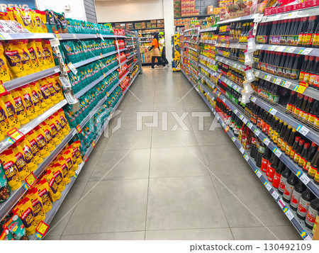 September 5, 2025. Surabaya, Indonesia. A shopper browsing supermarket aisles filled with canned food, sauces, and condiments under bright store lighting. September 5, 2025. Surabaya, Indonesia. A shopper browsing supermarket aisles filled with canned food, sauces, and condiments under bright store lighting. 130492109