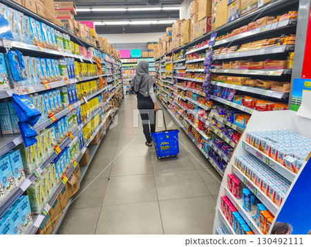 September 5, 2025. Surabaya, Indonesia. A shopper browsing supermarket aisles filled with canned food, sauces, and condiments under bright store lighting. September 5, 2025. Surabaya, Indonesia. A shopper browsing supermarket aisles filled with canned food, sauces, and condiments under bright store lighting. 130492111