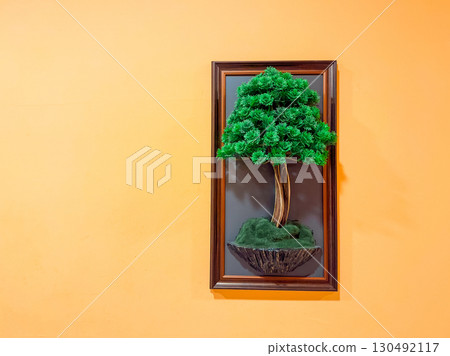 Framed green decorative tree artwork on orange wall with copy space. Design, decoration, and cultural lifestyle details in interior environment. 130492117