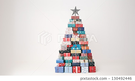 Many wrapped gift boxes forming a christmas tree shape stand in front of a white background, topped with a decorative star, creating a festive holiday scene 130492446