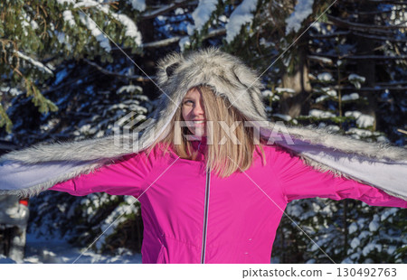 A girl enjoys a winter day in a snowy forest, wearing a furry hat and a bright pink jacket. 130492763