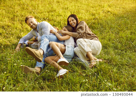 Laughing family lying on green grass and having fun in summer park together. Laughing family lying on green grass and having fun in summer park together. 130493044