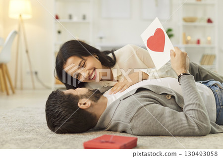 Happy couple lying on floor, hugging and celebrating Valentine Day or anniversary with gift at home. 130493058