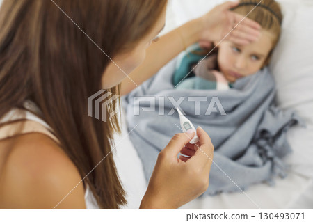 Mother checking temperature of sick child lying on bed at home suffering from flu or cold Mother checking temperature of sick child lying on bed at home suffering from flu or cold 130493071